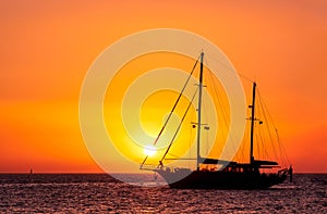 Silhouette of sailing boat with sails down against sun at sunset, sun glare on sea waters. Romantic seascape, sun touch