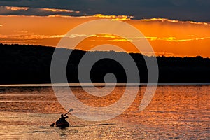 Silhouette of a sailor in a kayak canoe on the lake in the sunset light near an island