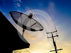 Silhouette of satellite dish and electrical post in the sunrise sky.