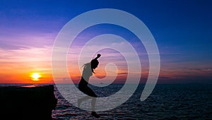 Silhouette of scared woman in the air falling from cliff into water at sunset