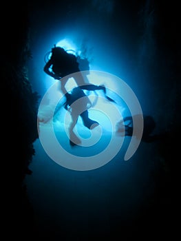 Silhouette of scuba divers in an underwater cave.