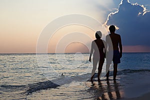 Silhouette Of Senior Couple Walking Along Beach At Sunset