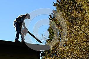 Silhouette of senior man with gas powered leaf blower cleaning roof gutters on an apartment building, fall maintenance