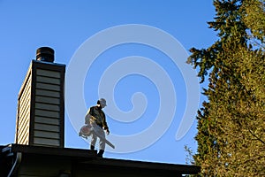Silhouette of senior man with gas powered leaf blower cleaning roof gutters on an apartment building, fall maintenance