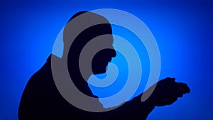 Silhouette of senior man play video game online. Male in profile with game console on blue background