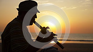 Silhouette of senior man playing bamboo flute on the beach at sunset