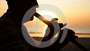 Silhouette of senior man playing bamboo flute on the beach at sunset