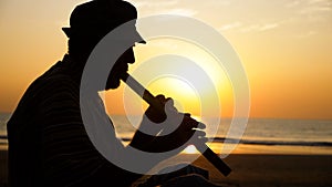 Silhouette of senior man playing bamboo flute on the beach at sunset