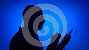 Silhouette of senior man put on ear-phones and listen to music on smart phone on blue background