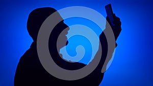 Silhouette of senior man use mobile phone on blue background. Male`s face in profile do selfie