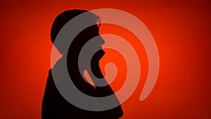 Silhouette of senior woman use cellphone on red background. Female`s face in profile talk on phone