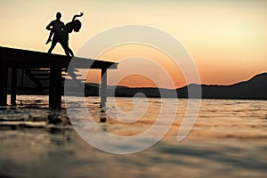 Silhouette of sensual couple dancing on pier with sunset above sea surface on background. Romance and love concept