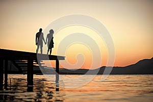 Silhouette of sensual couple stand on pier with sunset above sea surface on background. Couple in love on romantic date