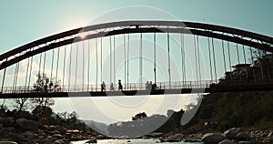 In a silhouette shot, individuals and a motorbike traverse a weathered iron bridge.