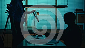 Silhouette shot of a perpetrator or prisoner sitting in the interrogation room in front of the detective. The policemnan photo