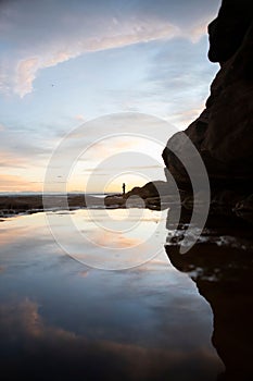 Silhouette shot of a person standing on a rocky beach while fishing in New South Wales, Australia