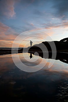 Silhouette shot of a person standing on a rocky beach while fishing in New South Wales, Australia