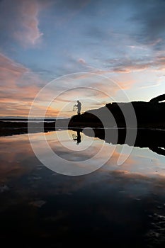 Silhouette shot of a person standing on a rocky beach while fishing in New South Wales, Australia