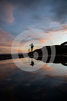 Silhouette shot of a person standing on a rocky beach while fishing in New South Wales, Australia