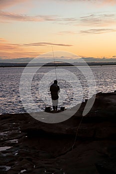 Silhouette shot of a person standing on a rocky beach while fishing in New South Wales, Australia