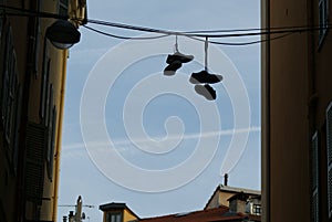 Silhouette shot of two pairs of shoes hanging on the wire attached to two opposite buildings.