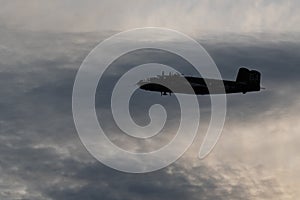 Silhouette shot of vintage military aircraft flying against a cloudy sky