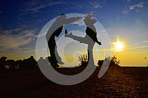 Silhouette Show the fight: Woman lift her leg and kick him to the tummy of a man at the mountain against the sunset