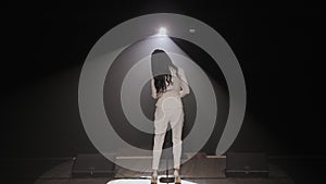 Silhouette of singer in dark on the stage under the light of a single spotlight.