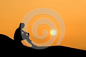 Silhouette of sitting man on rock at sunset