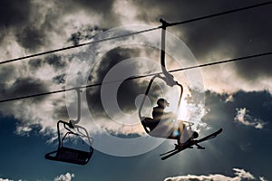 Silhouette of skiers sitting on ski-lift chairs