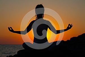 Silhouette of a slender fitness girl in the sun at sunset or sunrise in lotus pose.