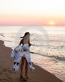 The silhouette of a slender tanned blonde with long hair in a black bikini, walks along the ocean