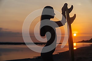 Silhouette of slim girl with surfboard in hands at beach on background of beautiful sunset