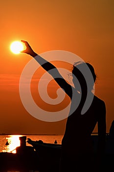 Silhouette of small girl holding sun during sunset above marina, part of motor boat visible on right side