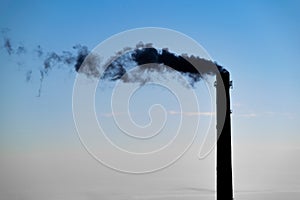 A silhouette of a smoking chimney with a sunset sky in the background