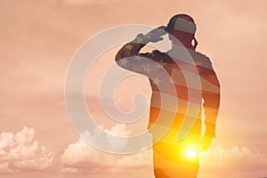 Silhouette of soldier with print of sunset and USA flag saluting on a background of light sky.