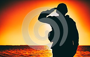 Silhouette of soldier salutes on sunset background