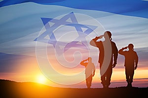 Silhouette of soldiers saluting against the sunrise in the desert and Israel flag.