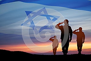 Silhouette of soldiers saluting against the sunrise in the desert and Israel flag.