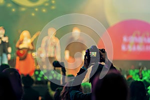 Silhouette of spectator, photographer taking picture with camera at concert, bright colorful light by stage lights