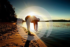 Silhouette of sport active adult man running and exercising on the beach. Calm water, island and sunny sky background.