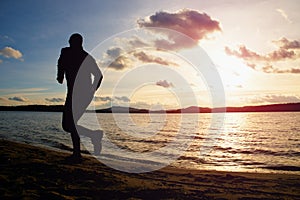 Silhouette of sport active man running and exercising on beach at vivid colorful sunset.