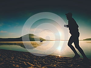 Silhouette of sport active man running on the lake beach at sunrise. Healthy lifestyle.