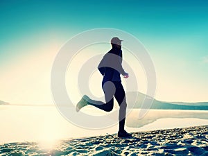 Silhouette of sport active man running on the lake beach at sunrise. Healthy lifestyle.