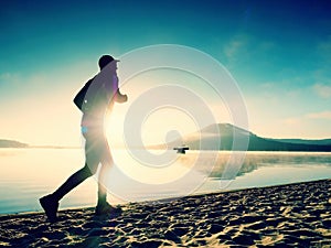 Silhouette of sport active man running on the lake beach at sunrise. Healthy lifestyle.