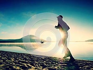 Silhouette of sport active man running on the lake beach at sunrise. Healthy lifestyle.