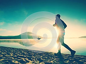 Silhouette of sport active man running on the lake beach at sunrise. Healthy lifestyle.