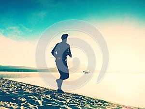 Silhouette of sport active man running on the lake beach at sunrise. Healthy lifestyle.