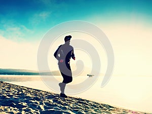 Silhouette of sport active man running on the lake beach at sunrise. Healthy lifestyle.