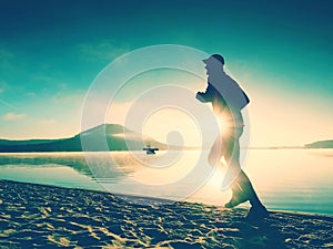 Silhouette of sport active man running on the lake beach at sunrise. Healthy lifestyle.